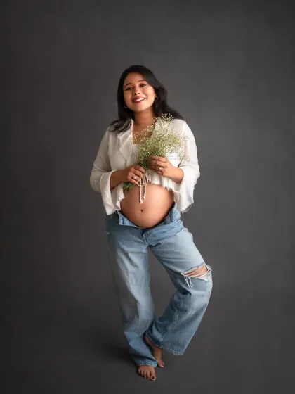 Your maternity shoot should feel like you. For a modern and relaxed vibe, we can go for a simple look like this, with a crop top and jeans against a clean backdrop, letting your beautiful bump be the star.