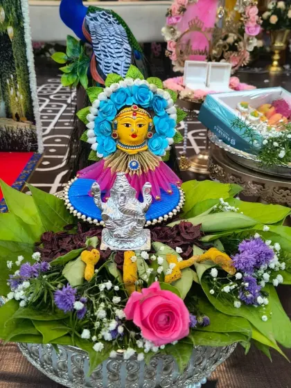 This is a beautifully arranged traditional offering plate, or thatte. It features a small deity figure, fresh flowers, and betel leaves, prepared for a puja or other religious ceremony.