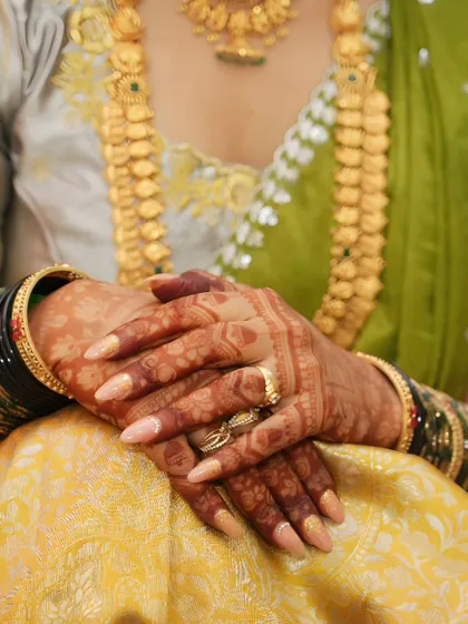 A close-up shot focusing on the hands, showcasing the beautiful contrast between the dark henna stain, the bride's jewelry, and her traditional saree.