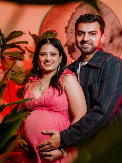 A classic couple's portrait from a maternity session. The couple smiles warmly for the camera, with the partner's arm gently around the mother-to-be, creating a picture of shared happiness and excitement.