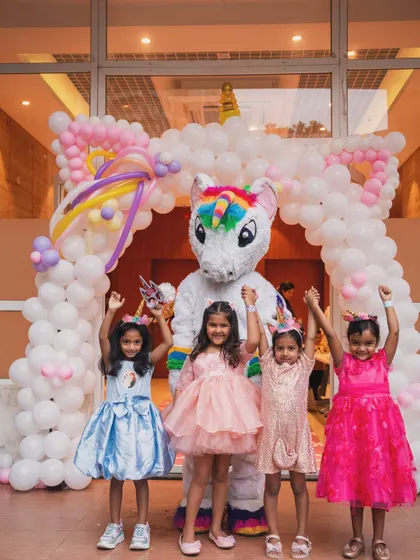 The birthday girl and her friends posing with a unicorn mascot, all raising their hands in celebration.