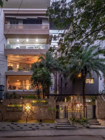 The facade of this apartment building in Jubilee Hills uses a monochromatic color palette that provides a sophisticated juxtaposition to the lush green landscape. The warm lighting creates an inviting atmosphere at night.
