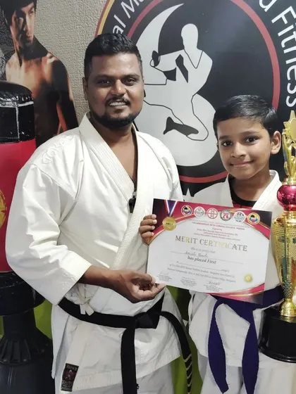 A proud moment for this purple belt student, holding his merit certificate and trophy after a successful karate competition.