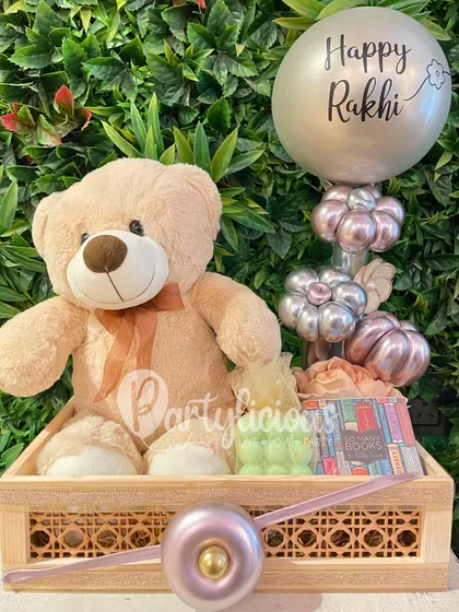 This adorable Rakhi gift basket is designed to deliver a big hug. It includes a soft teddy bear and other treats, all beautifully arranged in a stylish wooden crate and topped with a festive balloon.
