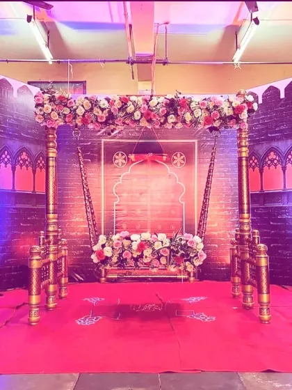 A traditional Maharashtrian-themed stage featuring an ornate wooden swing (jhula) decorated with flowers. The backdrop is designed to look like the walls of a fort, giving the ceremony a royal and cultural feel.