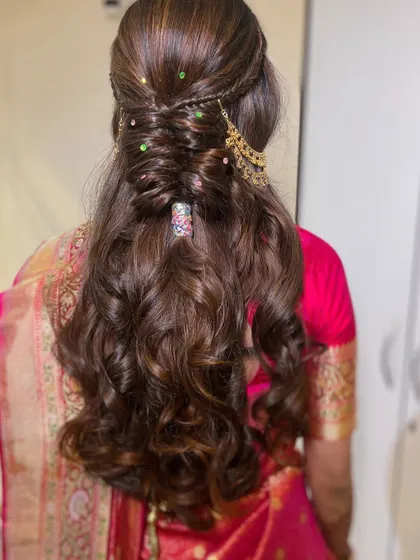 A modern take on a bridal hairstyle, featuring a half-up style with intricate braiding and loose curls, accented with colorful gems.