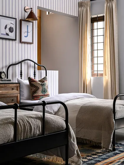 This is a view of the shared boys' bedroom, showing the twin black metal beds. I used a neutral striped wallpaper as a backdrop to keep the room from feeling too busy, while the patterned rug and pillows add color and a playful touch.