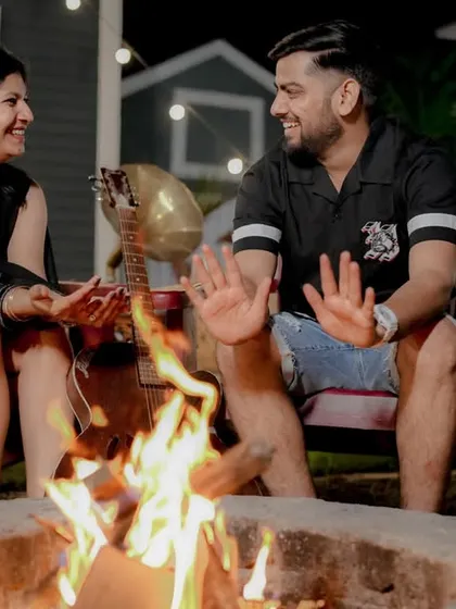 Cozying up by the bonfire for an evening pre-wedding shoot. The warm glow of the fire and the string lights create a magical and intimate atmosphere, perfect for romantic and relaxed photos.