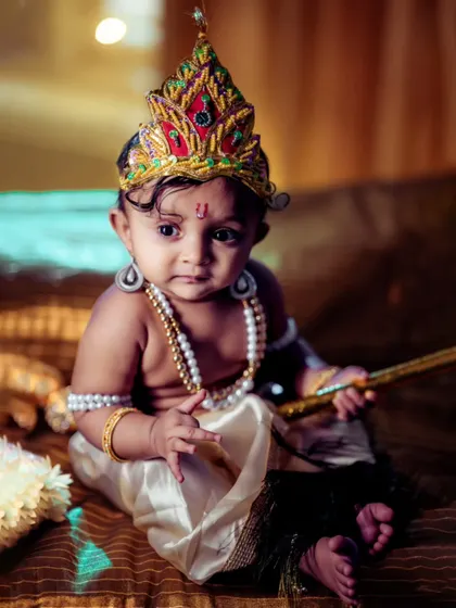 A thoughtful, seated portrait from our Little Krishna series. The composition focuses on the baby's calm demeanor and the rich details of the costume and props, creating a timeless and artistic image.