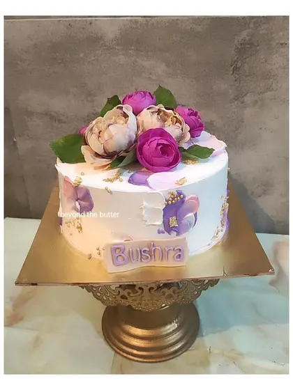 A lovely floral birthday cake with purple and pink sugar flowers, accented with gold leaf for a touch of sparkle.