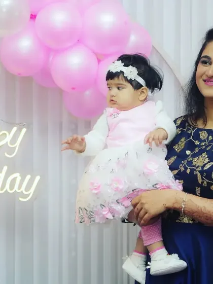 A mother holds her baby girl in front of a "Happy Birthday" sign. This photo beautifully combines the party atmosphere with a tender mother-daughter moment.