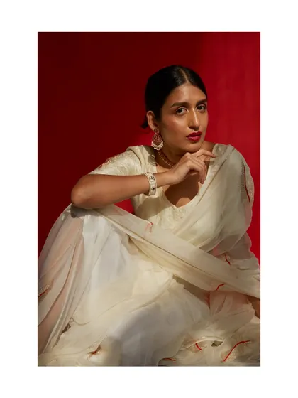 An elegant portrait for a saree brand. The combination of the off-white saree, bold red lip, and dramatic lighting against a red background is striking and memorable.