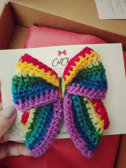 A butterfly-style rainbow bow, held up to show its unique shape and vibrant colors.