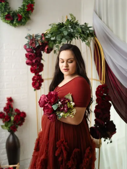 A serene portrait of the mother-to-be, surrounded by deep red flowers. The soft lighting and elegant gown create a truly timeless and artistic feel.