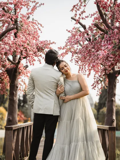 A serene pre-wedding moment captured on a bridge surrounded by cherry blossom-like trees. This showcases our ability to find picturesque natural settings for your shoot.