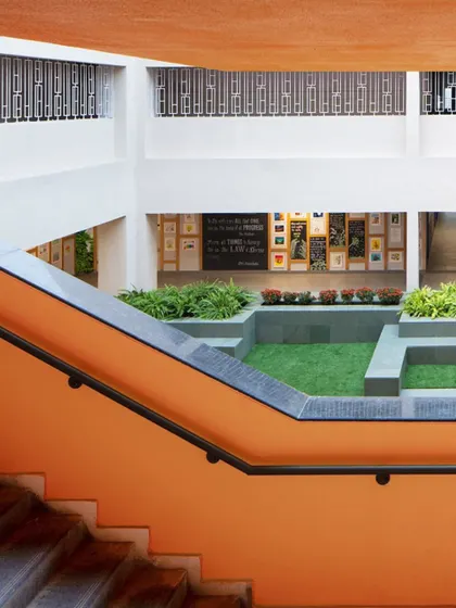 The interplay of the bright orange staircase against the neutral tones of the building and the green of the courtyard creates a dynamic and visually stimulating environment.