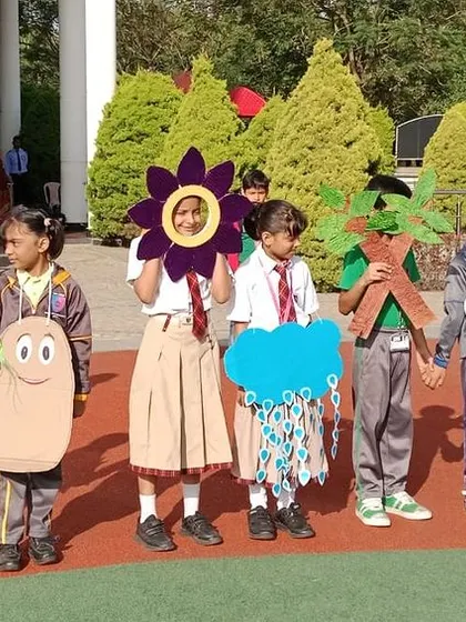 Students perform a captivating skit about seed germination during a school assembly, using creative costumes to represent the sun, a seed, and a flower.