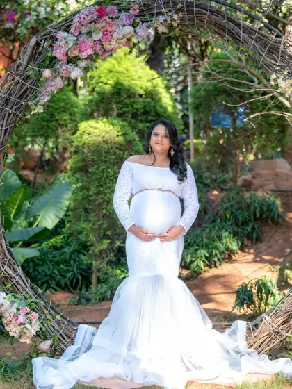 An angelic portrait of a mom-to-be in a white lace gown, framed by a rustic floral wreath.