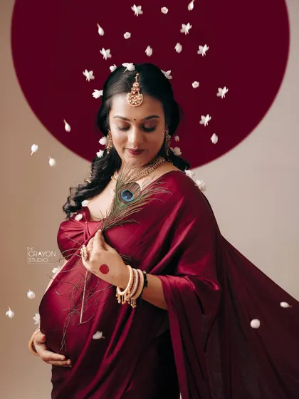 This is the art of waiting. In my studio, we used the deep red of a saree, a shower of soft petals, and traditional symbols like the peacock feather to create a portrait that feels like a timeless painting, honoring the universe growing within her.