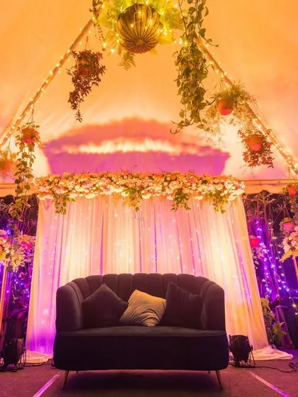 An intimate stage setup under a tent, illuminated with purple and orange lights, creating a cozy and magical ambiance for an evening event.