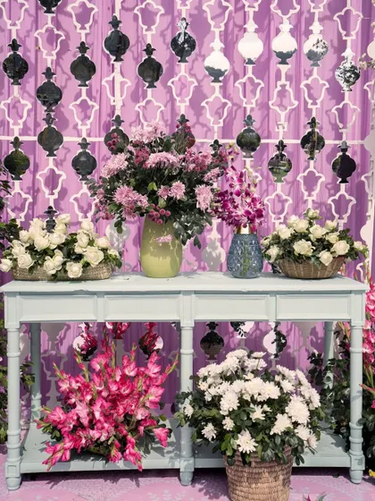 A beautifully styled console table at a lavender-themed event, featuring multiple floral arrangements and a decorative lattice backdrop.