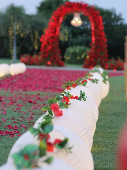 A close-up of the wedding aisle, lined with beautiful white paper lanterns and scattered red rose petals. This detail adds a soft, romantic glow to the walkway leading to the mandap.