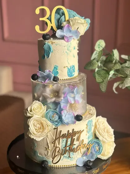 Dreamy layers in white and sky blue. This tall cake for a 30th birthday features a glowing light-up tier, delicate sugar flowers, and a beautiful textured finish.