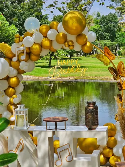 A glamorous birthday setup by the water. The gold and white balloon arch frames the view beautifully, creating a luxurious feel.