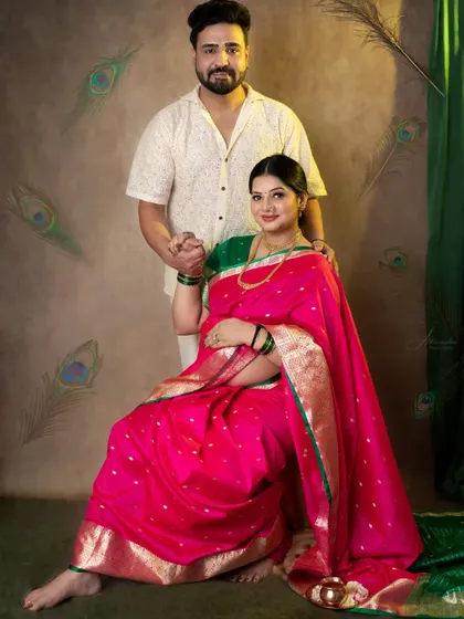 A classic and elegant portrait of the couple in their traditional outfits, set against a backdrop adorned with peacock feathers.
