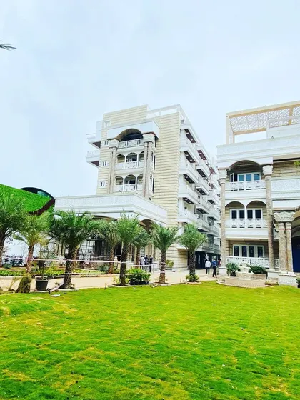 A wide shot of a large-scale residential project nearing completion. This shows the installation of a new lawn, mature palm trees, and the overall layout of a grand entrance landscape.