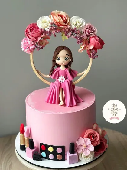 A chic cake for a makeup lover, featuring a fondant doll surrounded by edible lipstick, nail polish, and an eyeshadow palette.