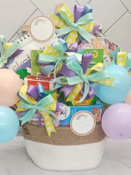 A custom art supplies gift basket for a creative star. This pastel-themed basket is filled with sketchbooks, crayons, and other art materials, topped with a balloon bouquet.
