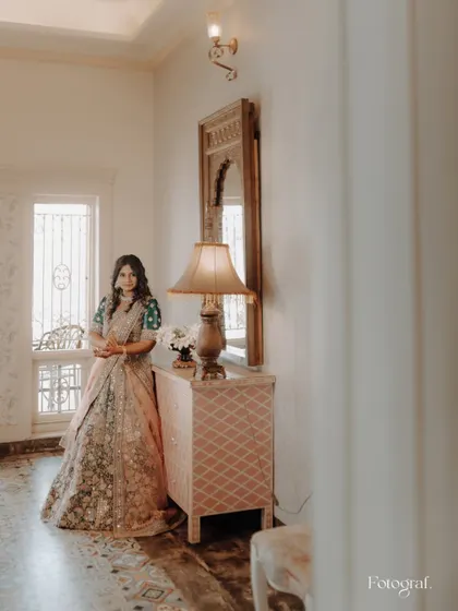 A bride in a soft-hued lehenga, standing in a beautifully decorated hallway. The portrait has a timeless and elegant feel.