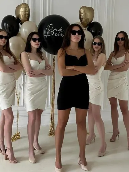 The bride tribe strikes a pose. A classic bachelorette party photo idea with the bride in black and her squad in white, complete with cool sunglasses and a "Bride Party" balloon.