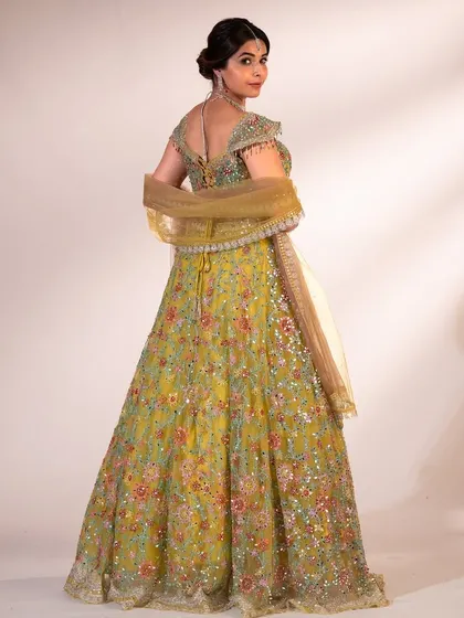 A back view of the lime green lehenga, showing the intricate tie-up detail of the blouse and the sheer, golden dupatta.