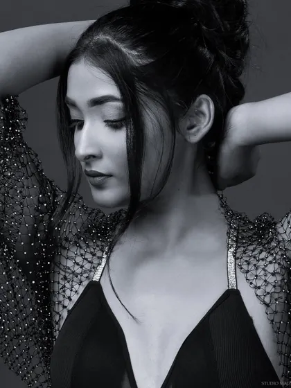 A black and white portrait of a model in a bralette and mesh shrug, with a soft, downward gaze.