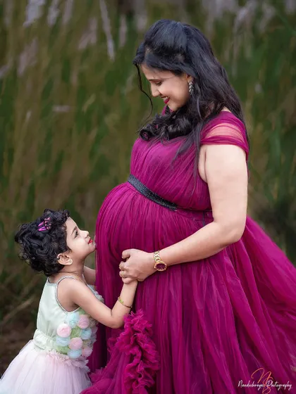 A precious moment between a mother and her daughter, who is looking up at her new sibling with wonder. Outdoor family maternity shoots are full of such sweet interactions.