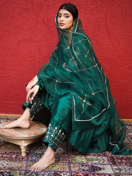 A direct and poised look, showcasing the full ensemble. The lighting is carefully controlled to bring out the sheen of the silk and the details of the embroidery against the bold red wall.