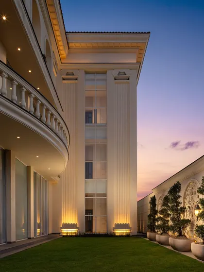 A view of a classical facade at sunset, with uplighting that accentuates the fluted columns and curved balcony. The soft colors of the sky complement the building's timeless elegance.