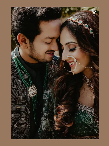 A close-up portrait of a couple in a tender embrace, highlighting the bride's joyful smile and beautiful nose ring. The rich colors of their outfits and jewelry are captured in exquisite detail.