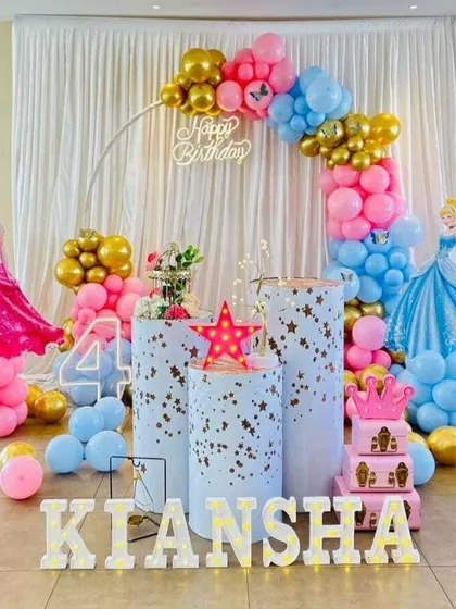 A Disney Princess first birthday party featuring Cinderella. The decor includes character cutouts, a circular balloon arch, and plinths decorated with stars.