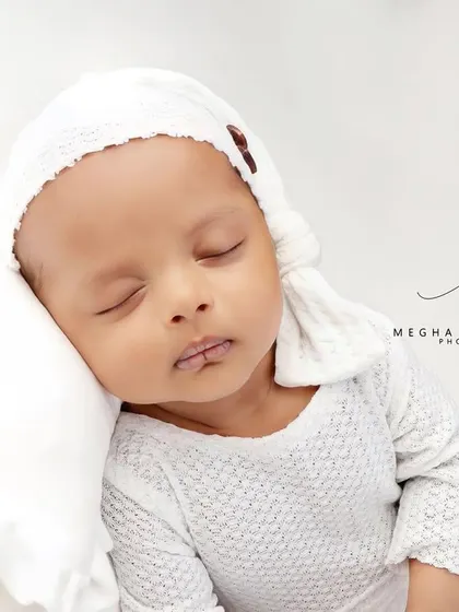 A close-up of the baby's face, resting on a soft white pillow.