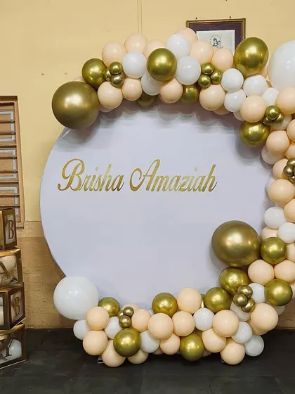 An elegant circular backdrop for a baby shower or naming ceremony. The white and gold balloon garland complements the gold "BABY" blocks on the side.