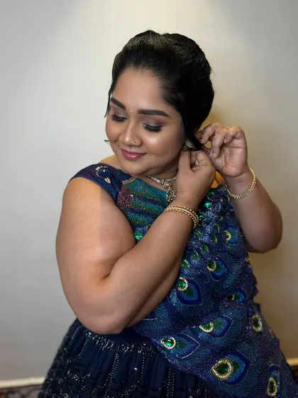 A candid moment of Nive putting on her earrings. The makeup is designed to look beautiful and last all day, ensuring she can enjoy the celebration without any worries.
