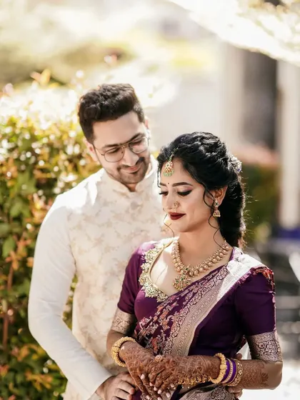 A romantic couple's portrait from their engagement. The bride's makeup is classic, with a deep lip color that complements her purple saree.