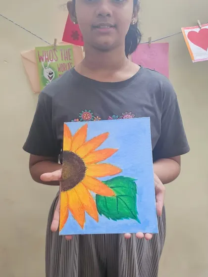 A student proudly holds up her completed acrylic painting of a sunflower. It's so rewarding to see them complete a project from start to finish.