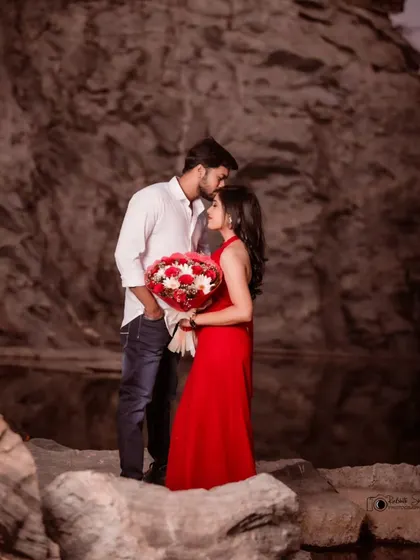 The groom's tender kiss on the bride's forehead is a classic romantic gesture. This pre-wedding photo, set against a dramatic natural backdrop, feels both intimate and epic.