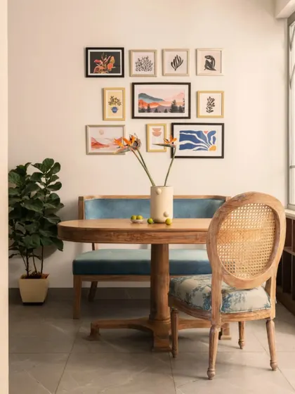 The dining nook is designed for both solo meals and intimate gatherings. A comfortable upholstered bench is paired with a classic cane-back chair, all centered around a gallery wall of art prints that reflect the client's personality.