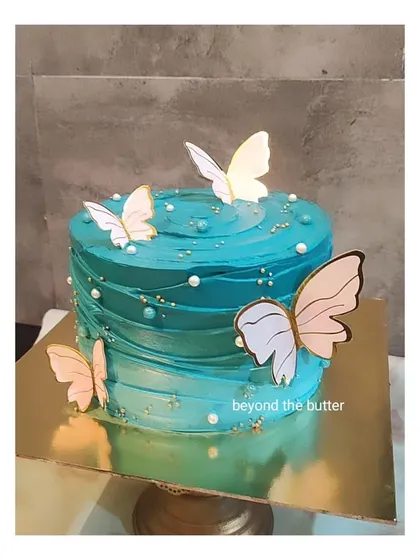 A teal blue butterfly cake with a beautiful swirl texture. The gold and white butterflies add a touch of elegance to the vibrant color.