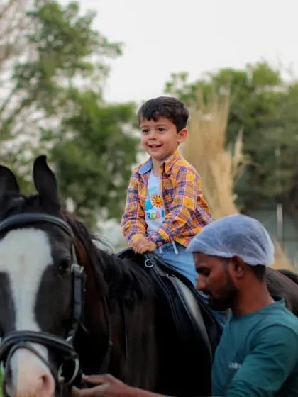 A beaming young boy enjoying a safe and guided horse ride at the farm.